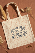 LOVED & FREE cream canvas tote bag flat lay on terracotta linen with botanical and doves design