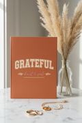 GRATEFUL terracotta spiral notebook upright on marble with pampas grass and gold necklace